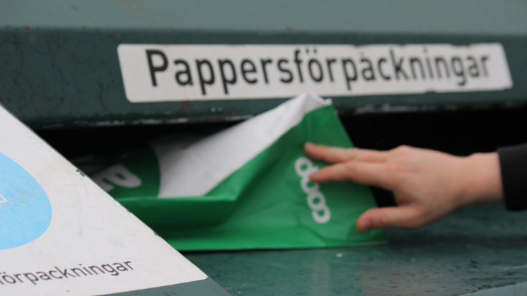person slänger papper i återvinningsstation