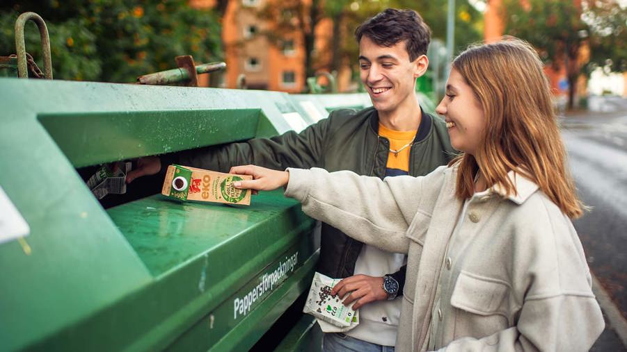 två unga personer slänger förpackning på en återvinningscentral